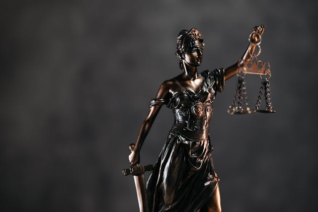 bronze-statue-of-lady-justice-holding-a-sword-and-balanced-scales-against-a-dark-background